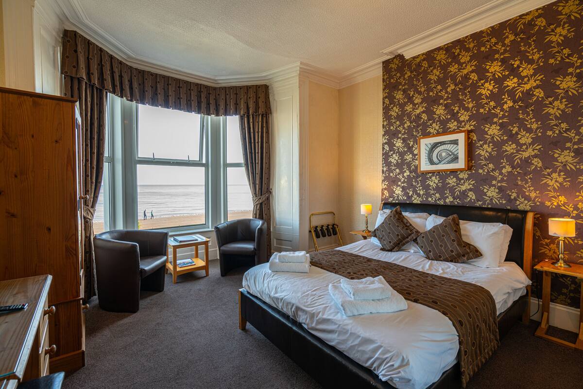 A hotel room with a large bed, a desk, a chair, and a view of the beach.
