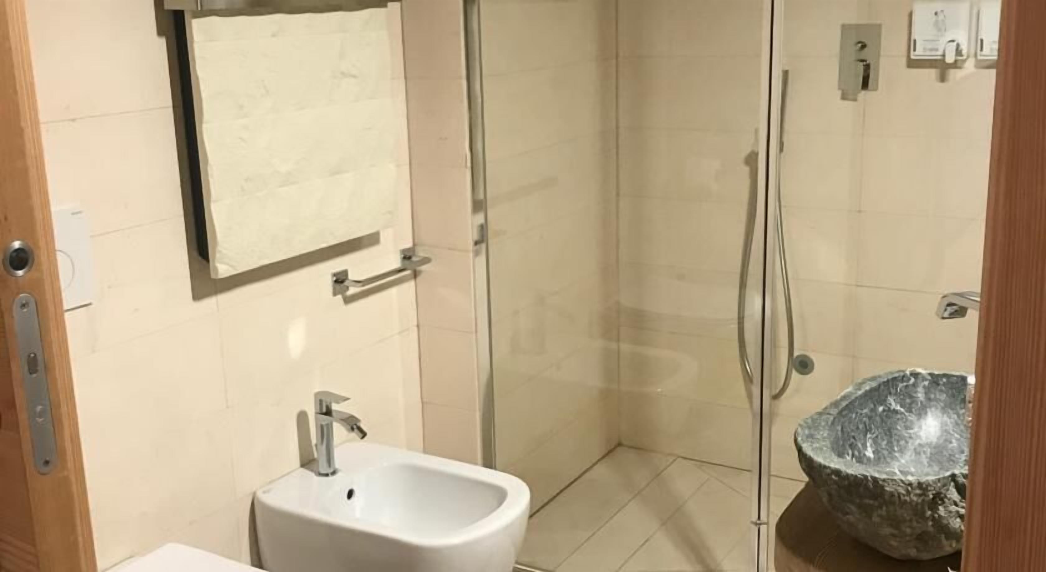 A bathroom with a sink, mirror, towel rack, shower, and a stone basin.