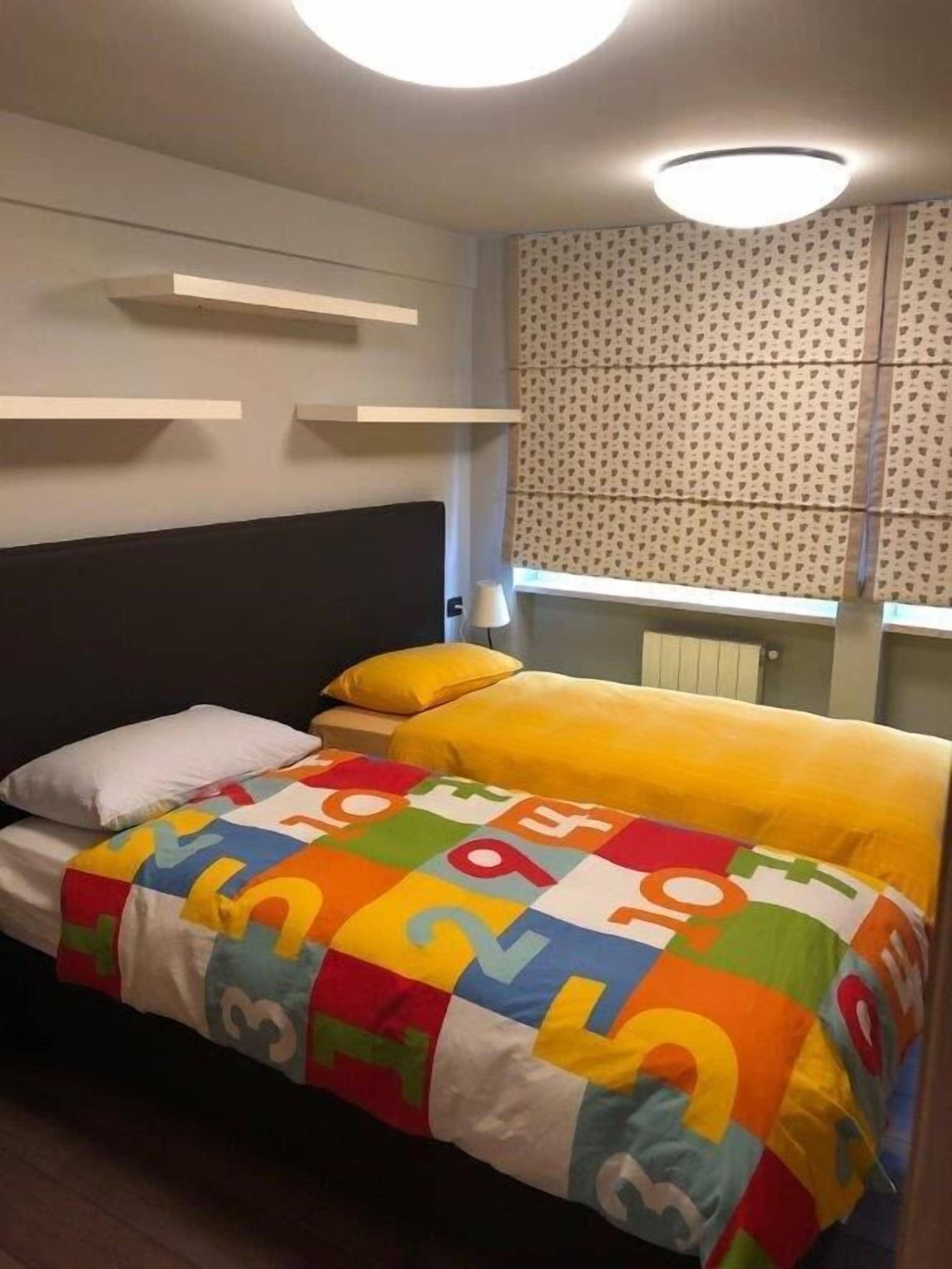 Una cama con un edredón colorido, un cabecero y una ventana con cortinas estampadas.