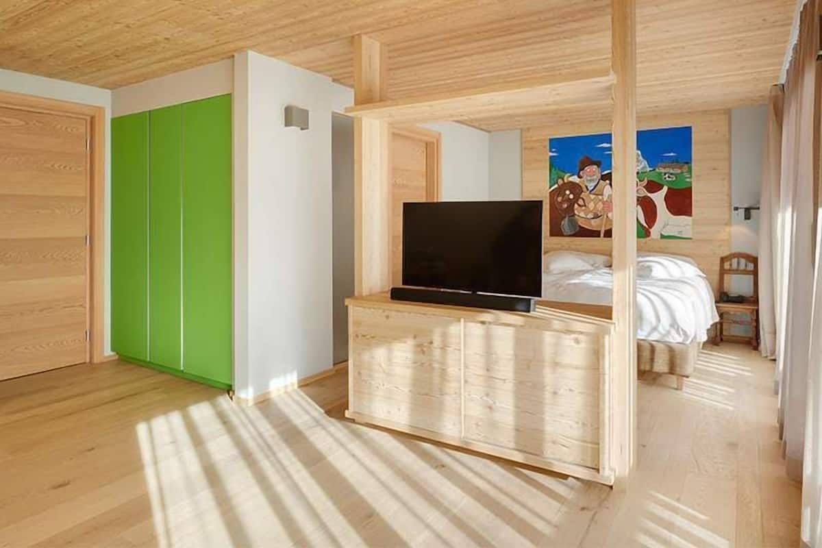 Ein Zimmer mit Holzbalkendecke, einem grünen Kleiderschrank, einem Bett mit weißer Bettwäsche und einem Fernseher auf einem Holztisch.