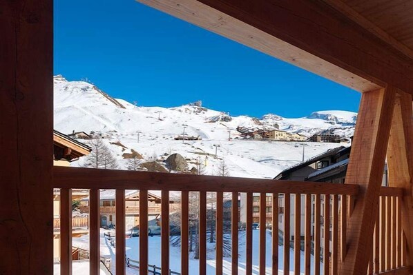 A wooden balcony with a view of a snowy mountain landscape and buildings. - Aux Pieds du Roi (Valtournenche)