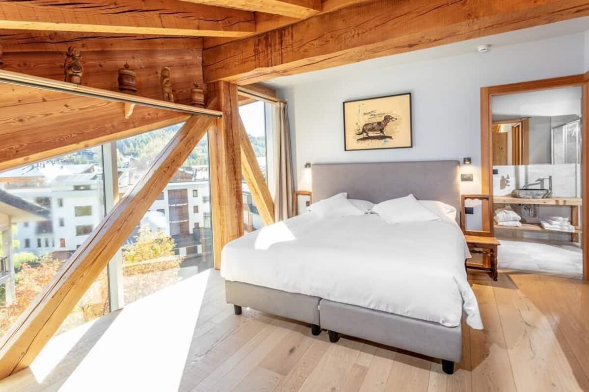 Ein Schlafzimmer mit einem großen Bett, Holzbalken, einem Oberlicht und Blick auf die Stadt.