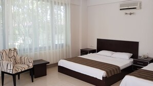 Una habitación de hotel con una cama grande, una silla, una mesita de noche y un equipo de aire acondicionado.