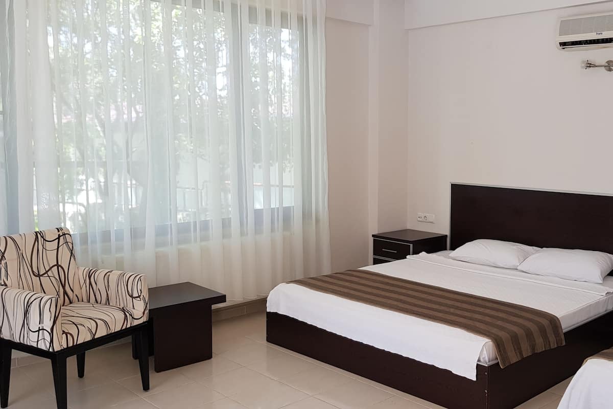 Une chambre d’hôtel avec un grand lit, une chaise, une table de chevet et un climatiseur.