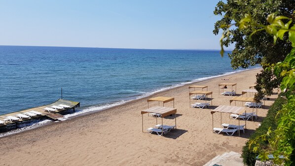 Una playa con tumbonas y sombrillas, una terraza de madera y una vista despejada del mar.