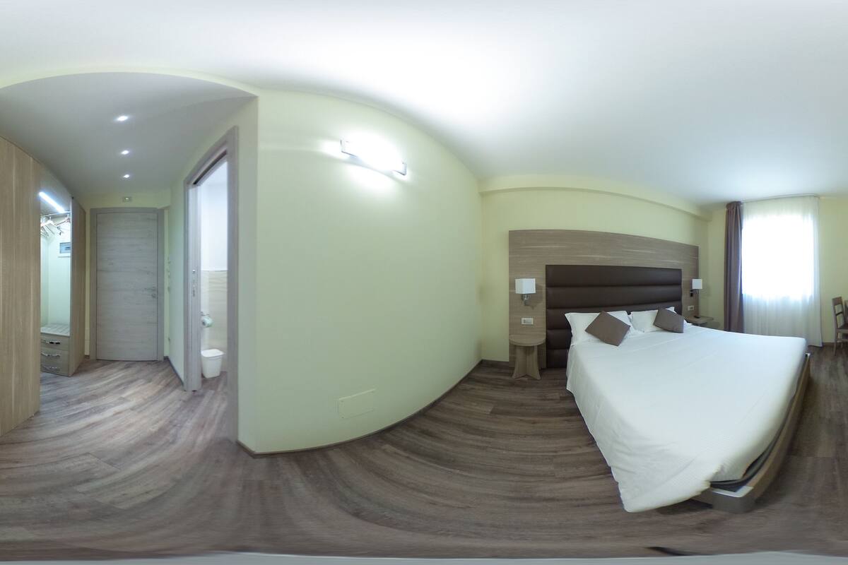 A panoramic view of a hotel room with a large bed, bedside tables, a desk, and a TV mounted on the wall.