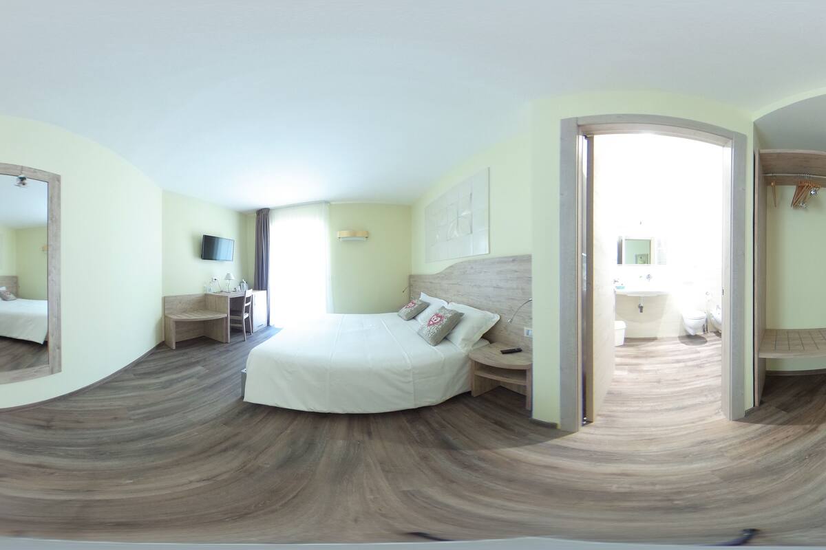 A modern bedroom with a curved ceiling, a large bed, a bedside table, a mirror, and a view into the bathroom.