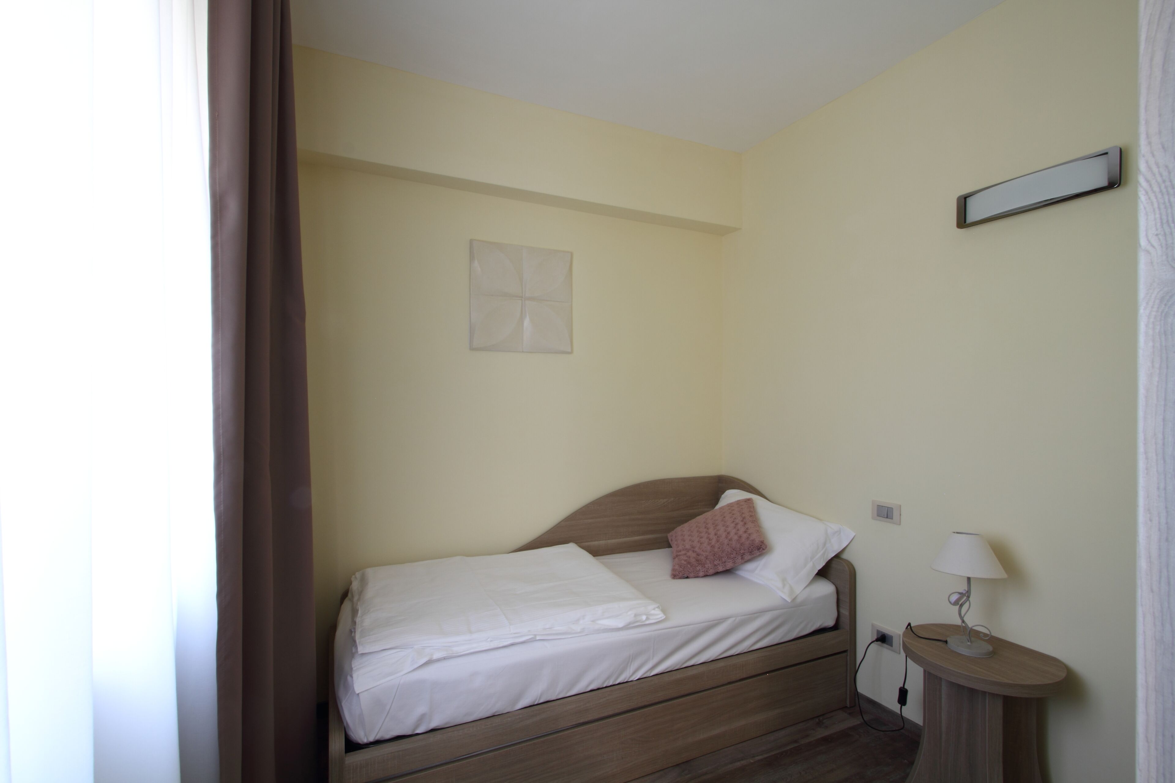 Un lit simple avec une tête de lit en bois, une table de chevet avec une lampe et un luminaire fixé au mur.