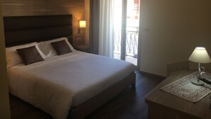 Habitación de hotel con una cama grande, una mesita de noche con lámpara, una ventana con cortinas y vistas al balcón exterior.