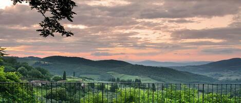 A balcony with two chairs and a table, overlooking a lush valley with a metal railing.