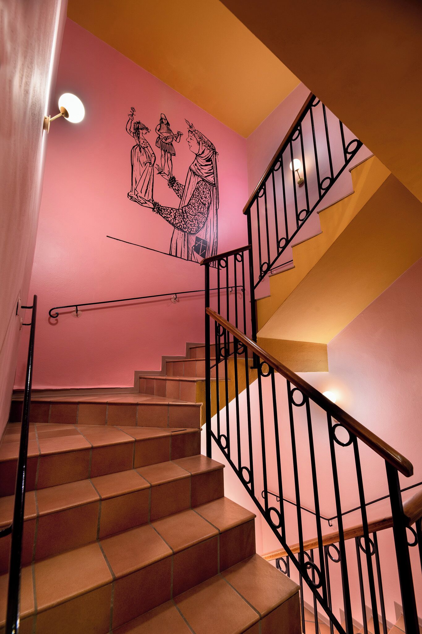 A staircase with a pink wall and a black railing.
