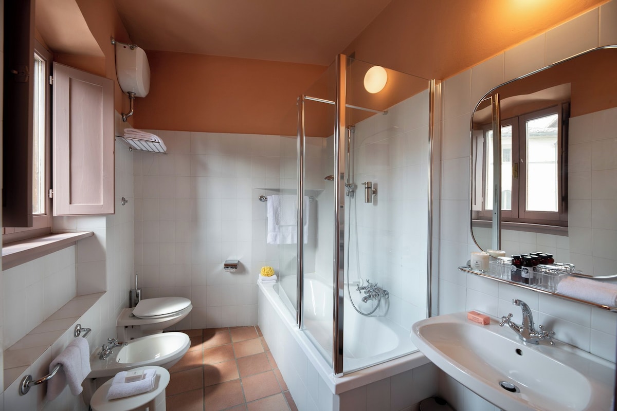 A modern bathroom with a bathtub, two sinks, a toilet, and a glass-enclosed shower.