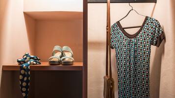 A closet with a pair of sandals and a blue polka-dotted scarf on a shelf, and a blue and black patterned dress hanging on a rod.