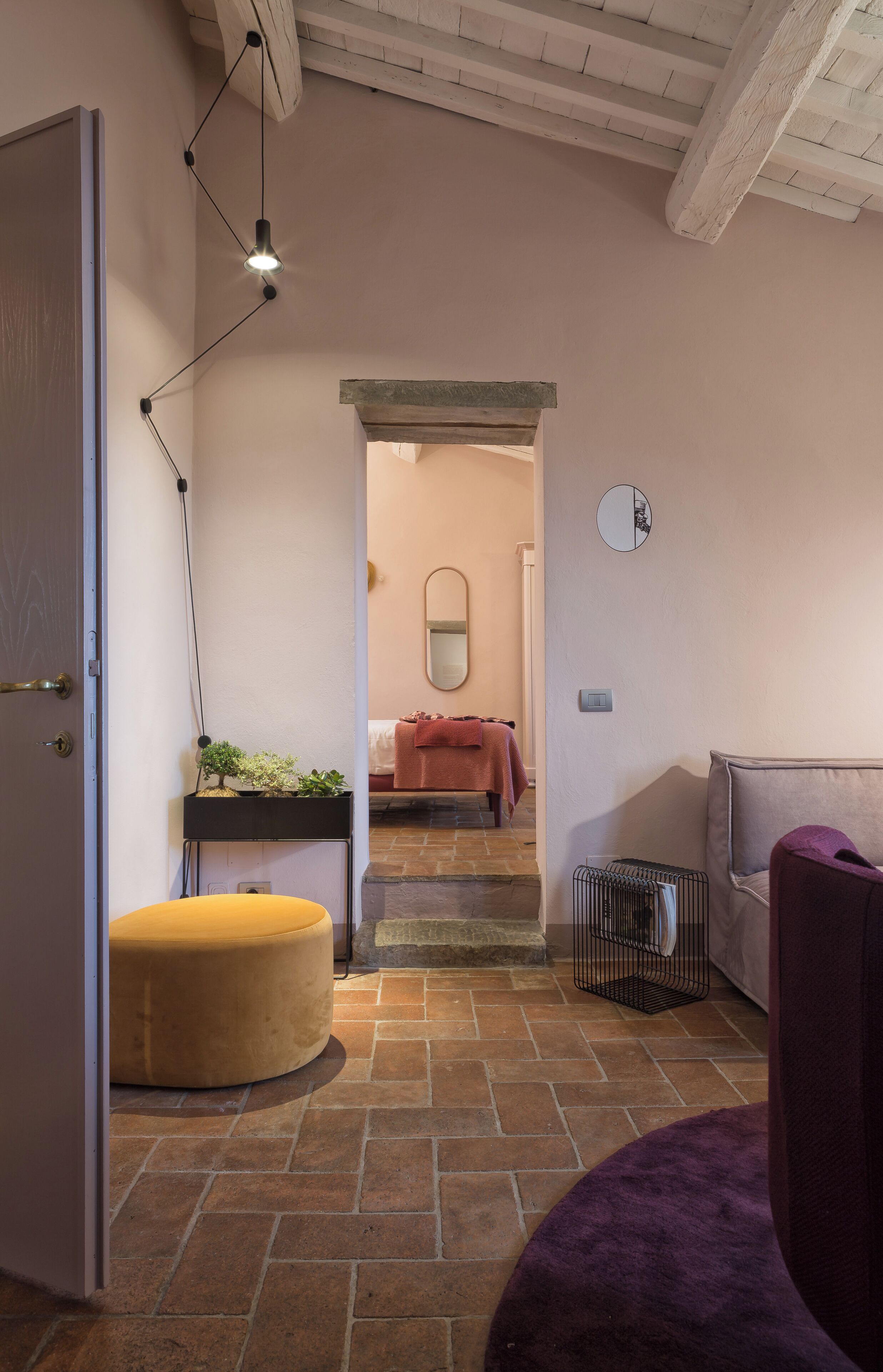 A hallway with a bed, a mirror, and a small plant.