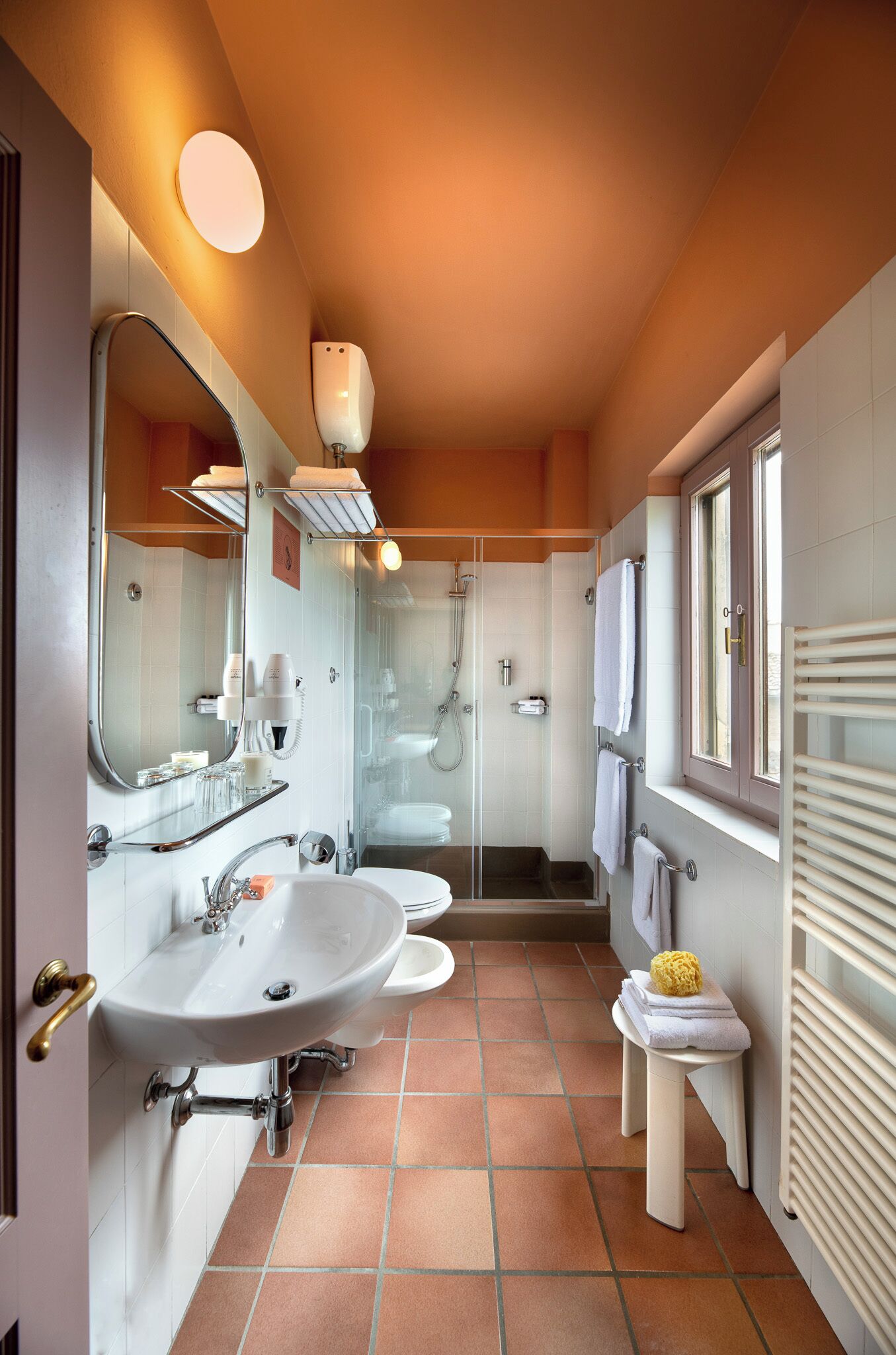 A modern bathroom with a large mirror, two sinks, a shower, and a window.