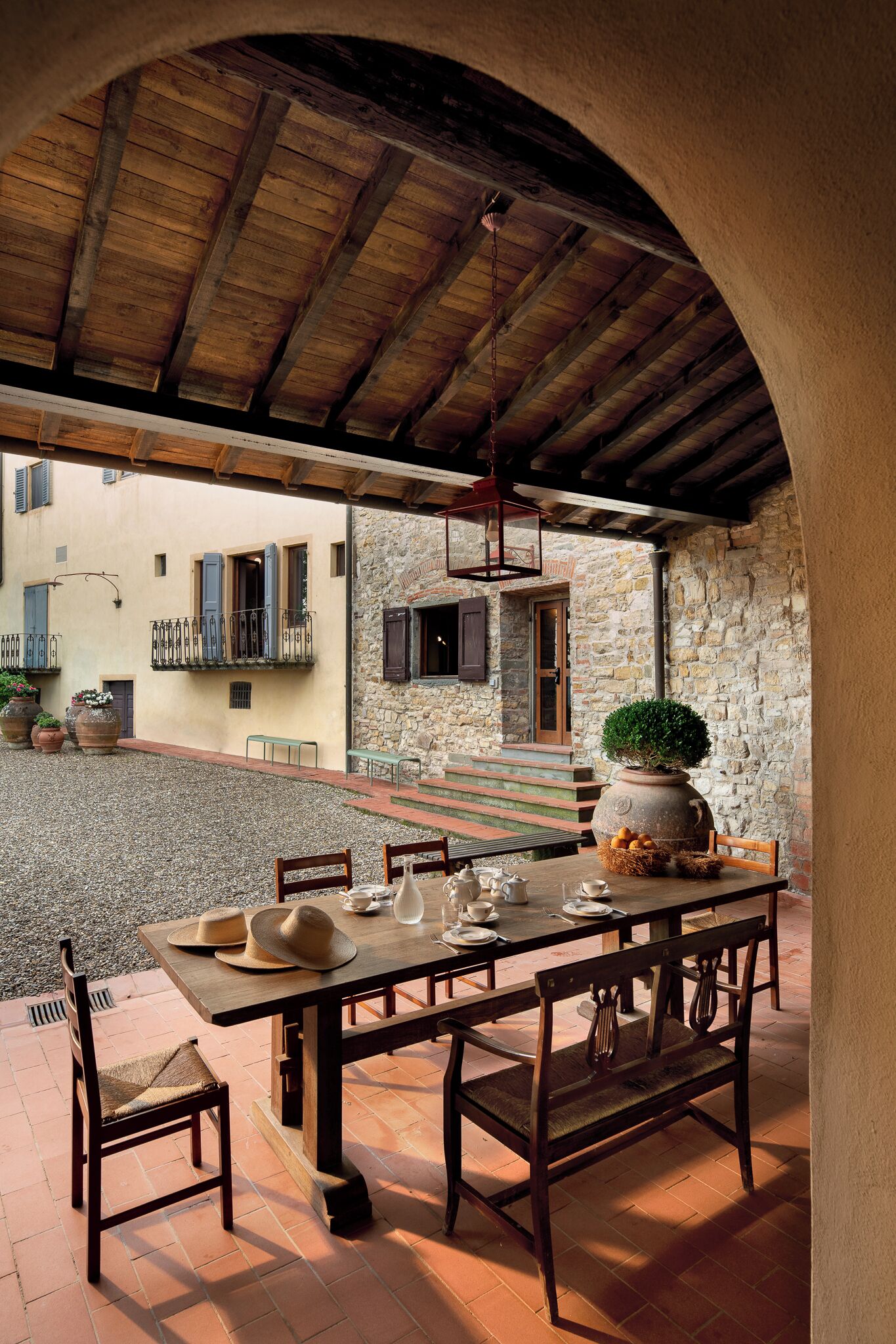 An outdoor dining area with a rustic stone wall, wooden table, chairs, and a potted plant.