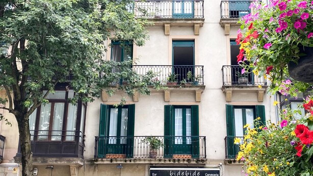 A building with multiple balconies, green shutters, and a storefront named 'bidebide'. - Pensión Urkia (San Sebastián)