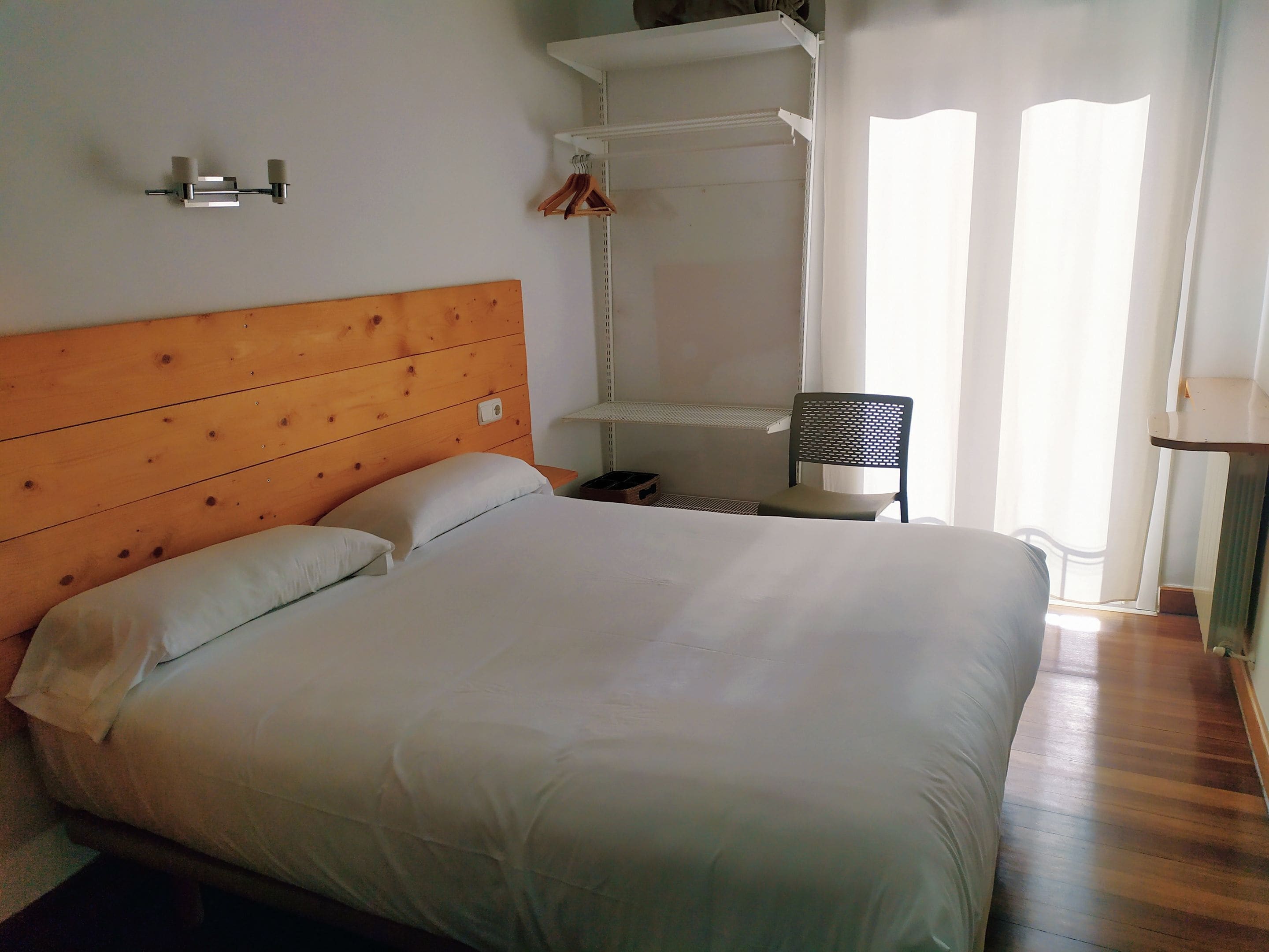 A neatly made bed with a wooden headboard, a bedside table with a lamp, and a chair.