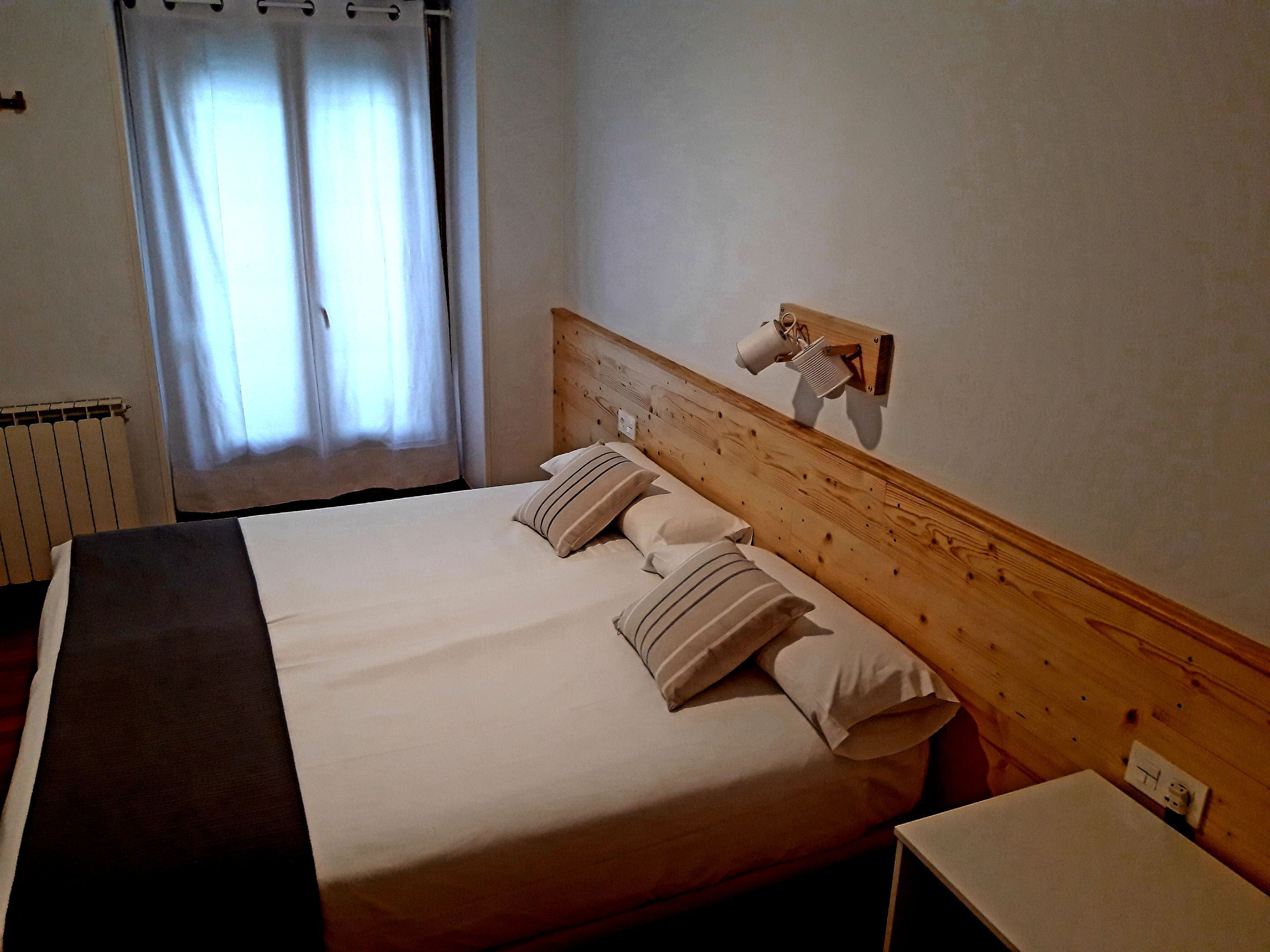 A neatly made bed with a wooden headboard, a bedside table, and a wall-mounted lamp.