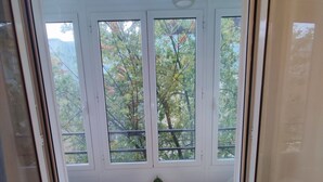 A room with a wooden floor, white walls, and a large window with multiple panes. There is a small round table with a white chair in front of the window. - Pensión Urkia (San Sebastián)