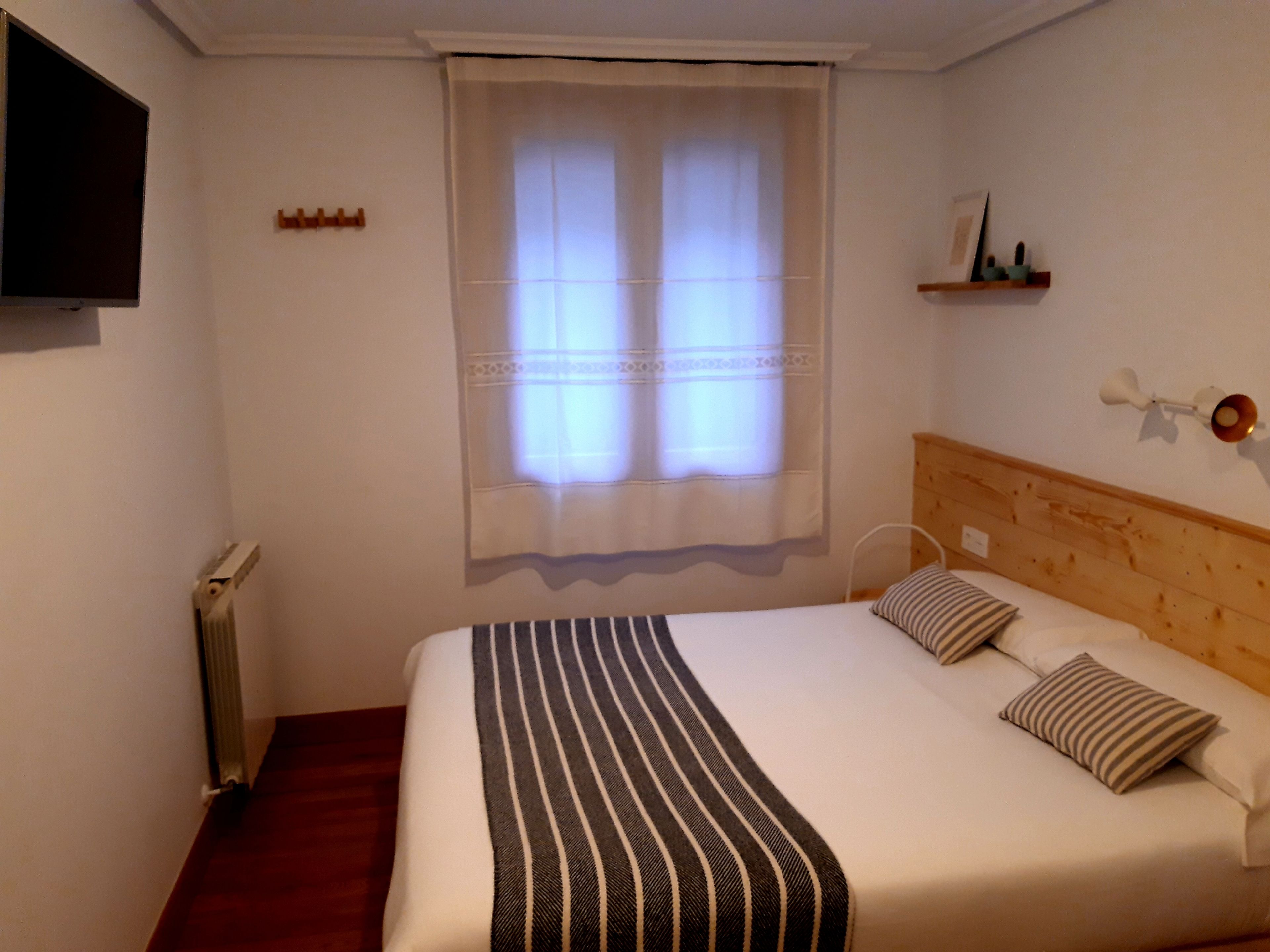 A bedroom with a bed, a window with curtains, a mounted TV, and a wooden headboard.
