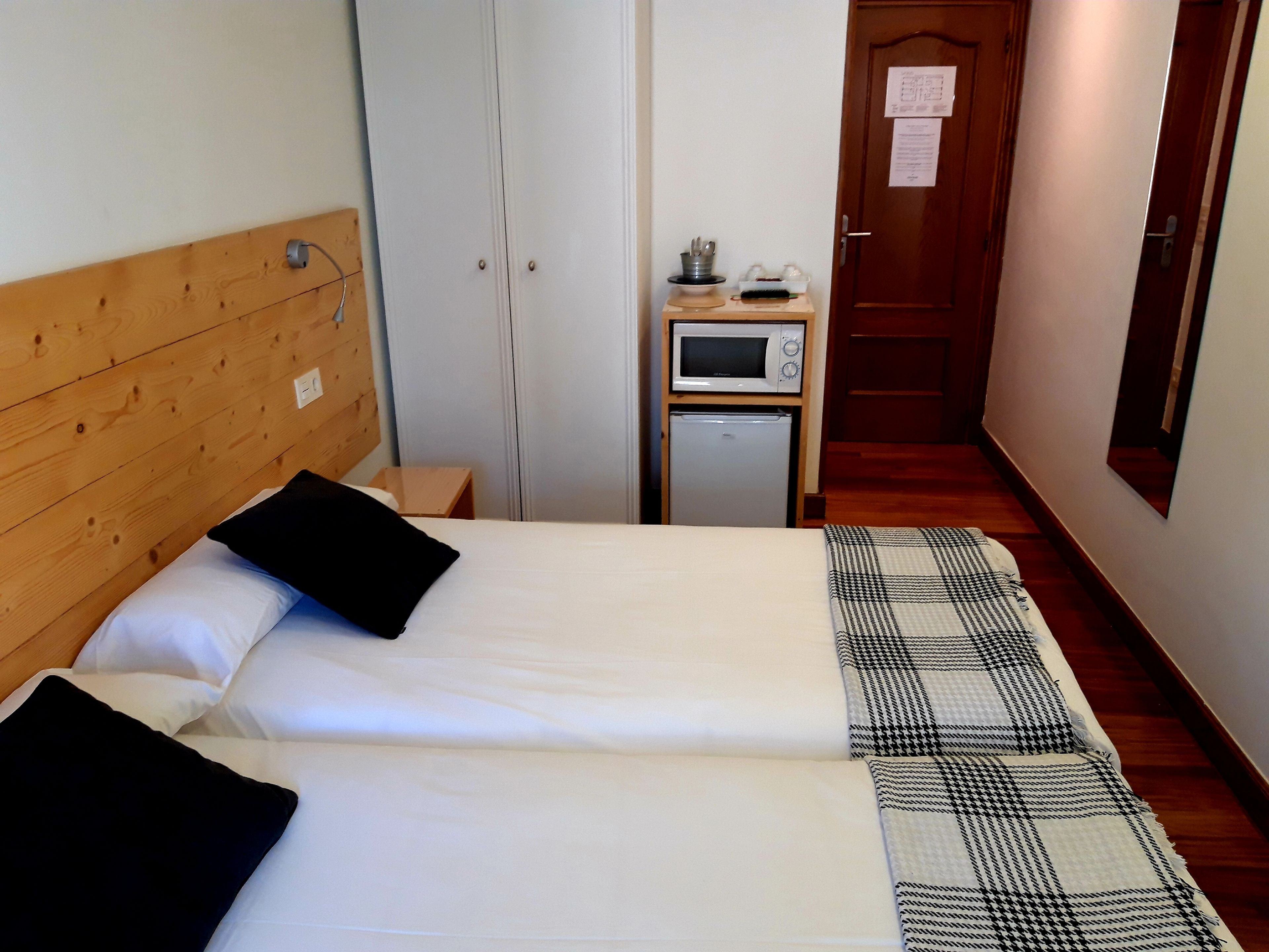 A hotel room with two beds, a wooden headboard, a small table with a microwave and refrigerator, and a door with a notice.