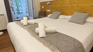 A hotel room with a large bed, wooden headboard, and a view through a door to the outside. - Pensión Urkia (San Sebastián)