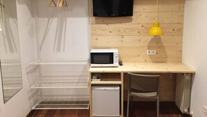 A compact room with a wooden desk, a small refrigerator, a microwave, a chair, and a TV mounted on the wall. - Pensión Urkia (San Sebastián)