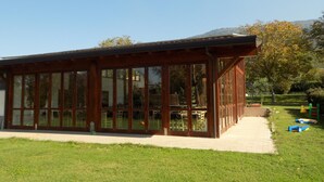 Een houten paviljoen met grote glasramen, gelegen op een gazon met een berg op de achtergrond.