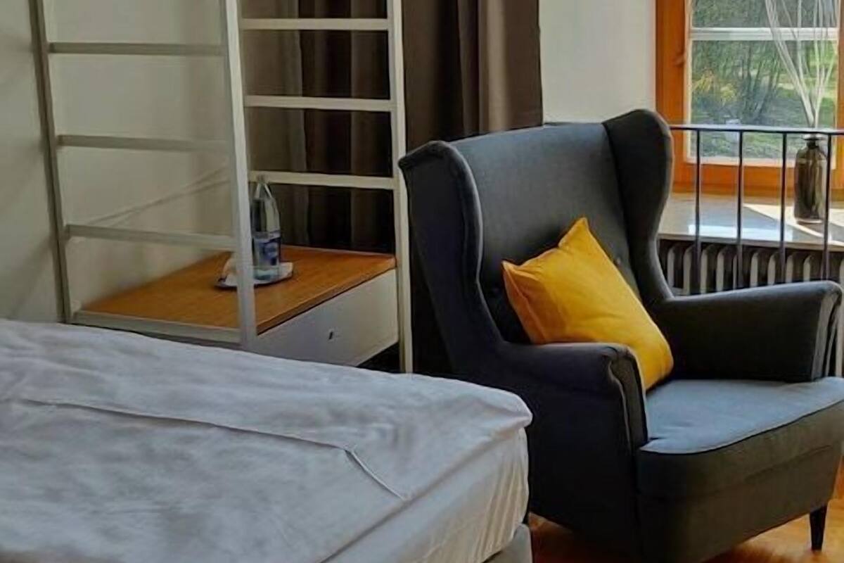 A bedroom with a bed, a chair, a wardrobe, a window, and a lamp.