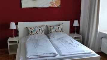 Ein Schlafzimmer mit einem großen Bett, zwei Nachttischen, einer roten Wand und einem Gemälde über dem Bett.
