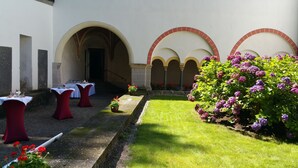 An outdoor dining area with tables and chairs, surrounded by a garden with flowers and a pathway. - Gästehaus Abtei Sayn (Bendorf)