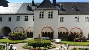 A building with a symmetrical facade, arched windows, and a central courtyard with benches and flower beds. - Gästehaus Abtei Sayn (Bendorf)