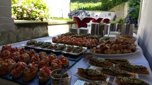 Une table de buffet proposant divers amuse-gueules et un espace repas avec des chaises rouges et une nappe blanche.