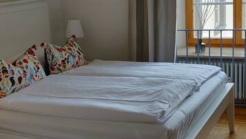 A bedroom with a large bed, a hanging black lamp, a window with curtains, and a wooden floor.