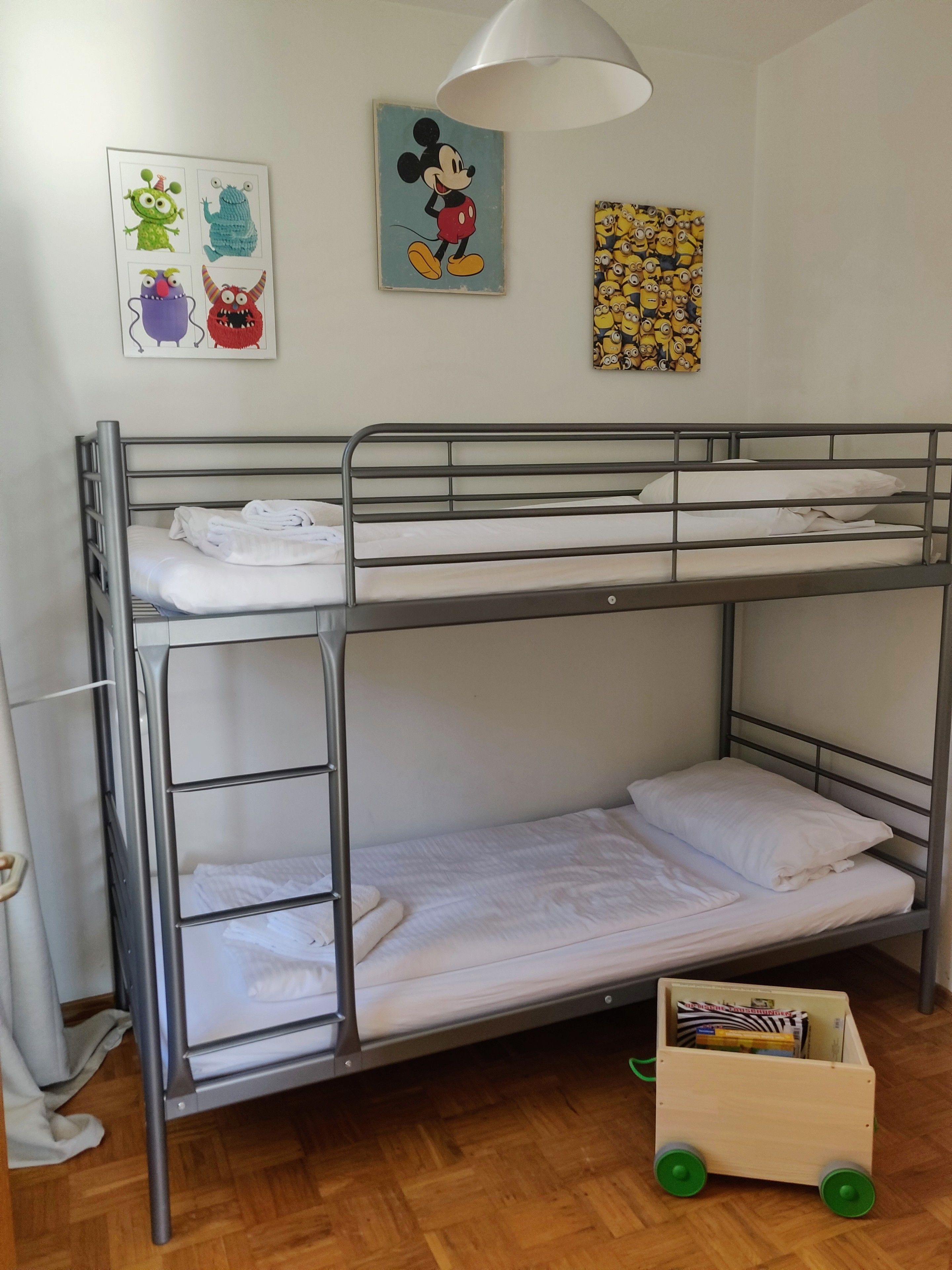 Una litera con ropa de cama blanca, un coche de juguete de madera y decoración en la pared con personajes de caricaturas.