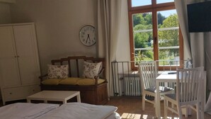 A bedroom with a bed, a desk, a chair, a window with curtains, a radiator, and a clock on the wall. - Gästehaus Abtei Sayn (Bendorf)
