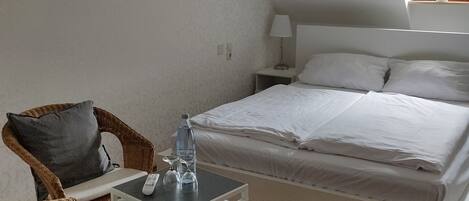 A bedroom with a bed, a nightstand, a table, a chair, and a potted plant.