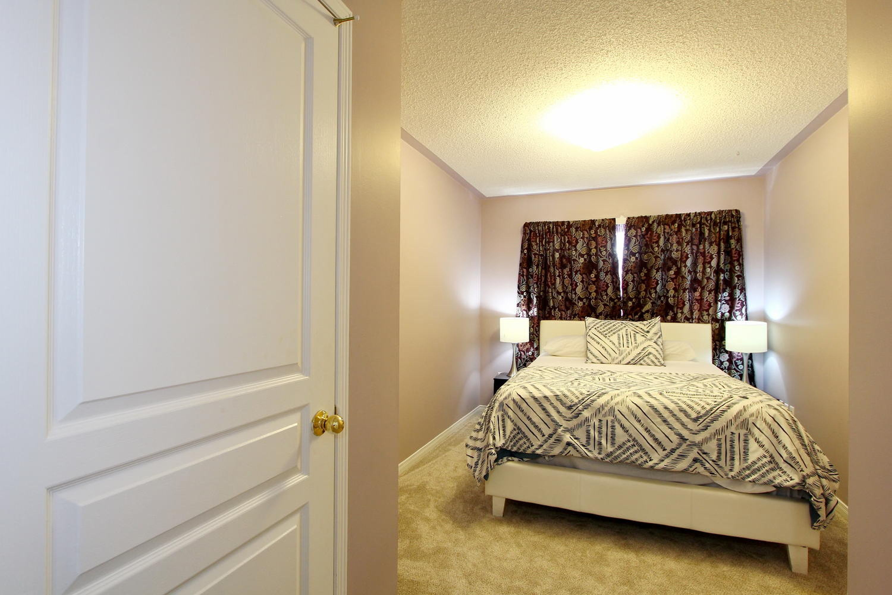 A bedroom with a bed, two bedside lamps, and a door.