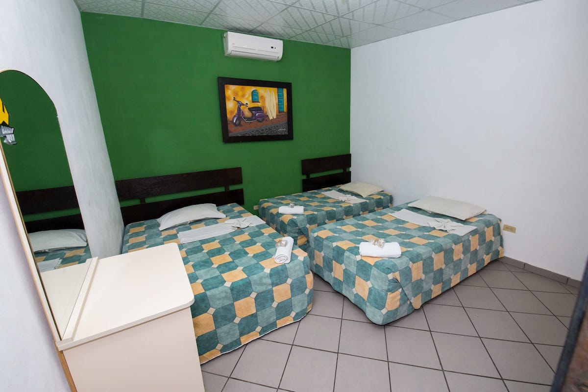 A room with three beds, each with a checkered bedspread, a white desk, and a green wall with a framed picture.