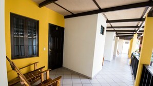 A hallway with a wooden bench, a black door, and a yellow wall. - Papaya'S Lodge (Tamanique)