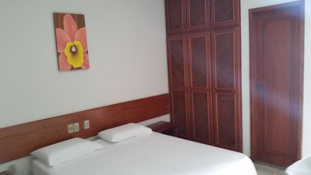 A hotel room with a bed, a wooden headboard, a wall-mounted artwork, and a wooden wardrobe.