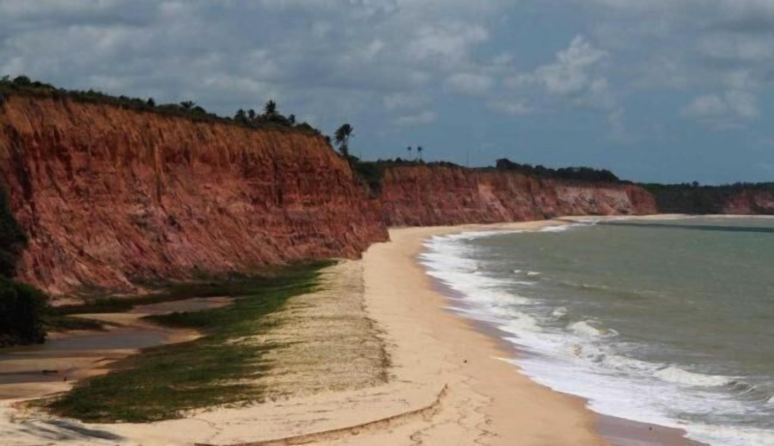 A coastal beach with a sandy shore, a cliff, and a clear sky.