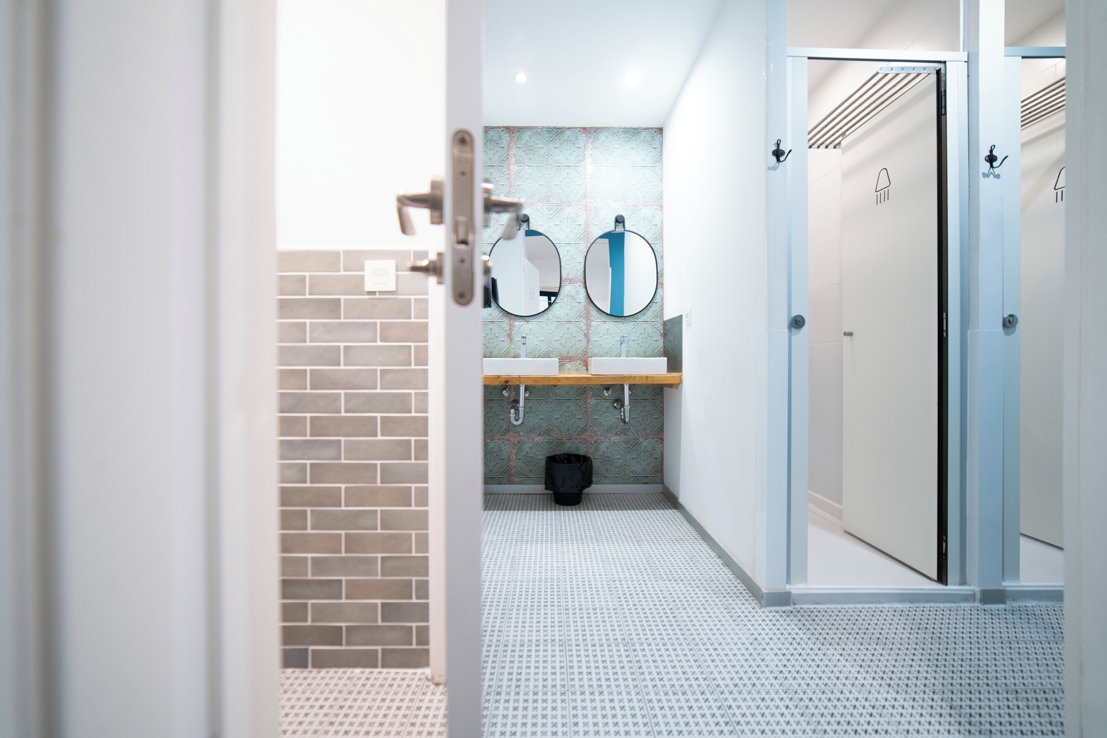 A modern bathroom with a tiled floor, a sink, two mirrors, and a door.
