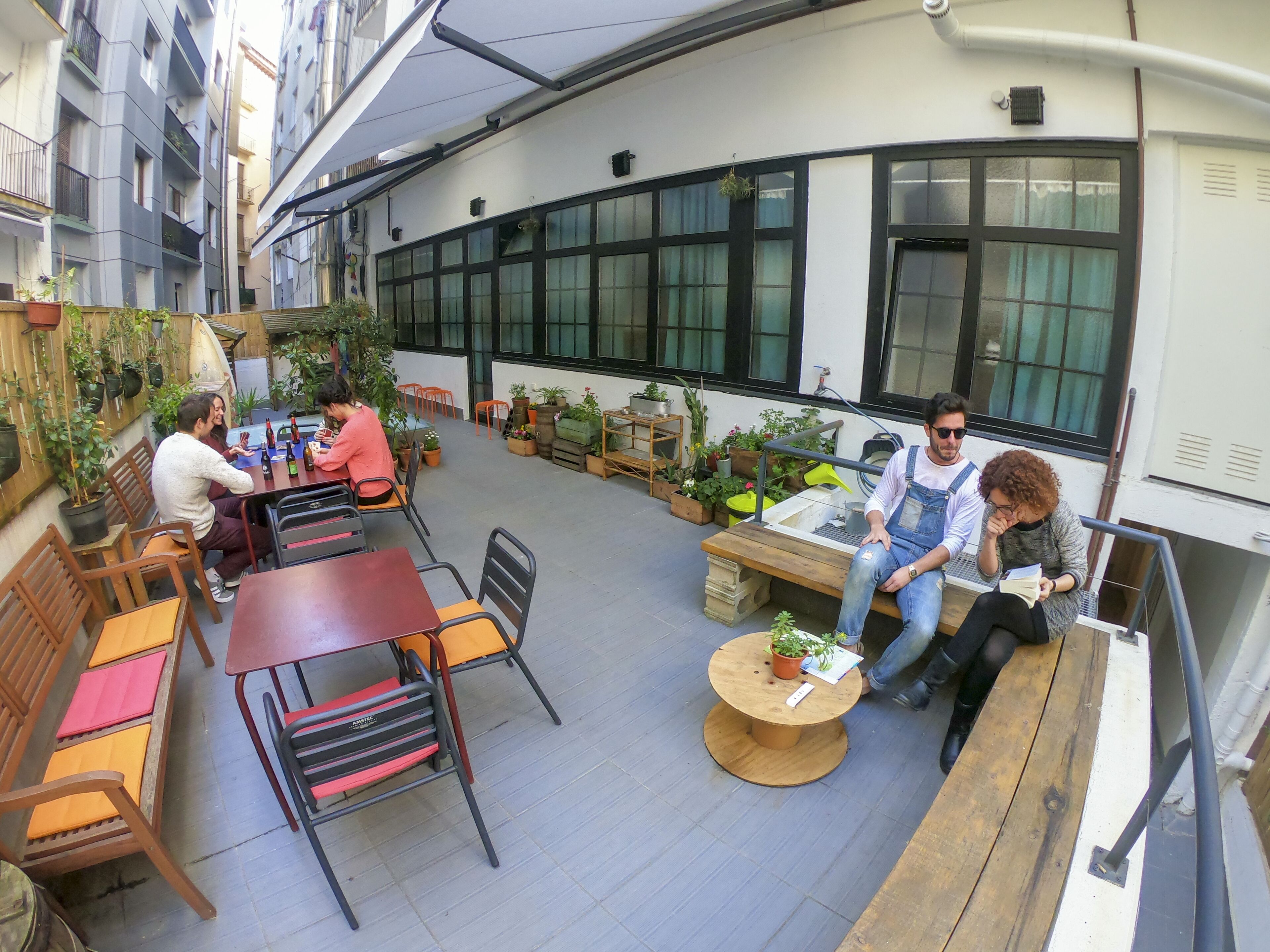 An outdoor patio area with tables and chairs, surrounded by potted plants and a view of a building with large windows.