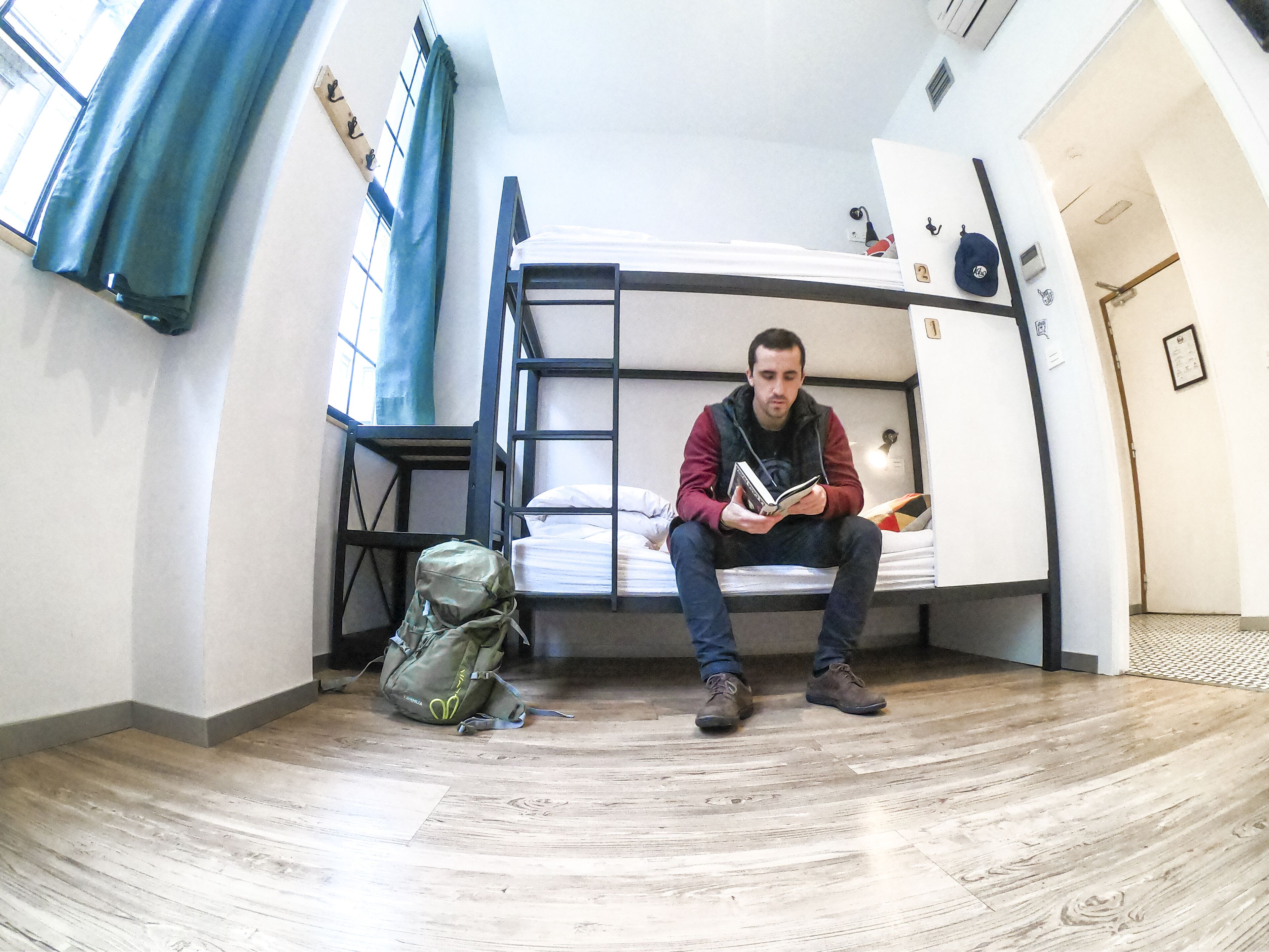 A bunk bed room with a person sitting on the lower bunk reading a book.