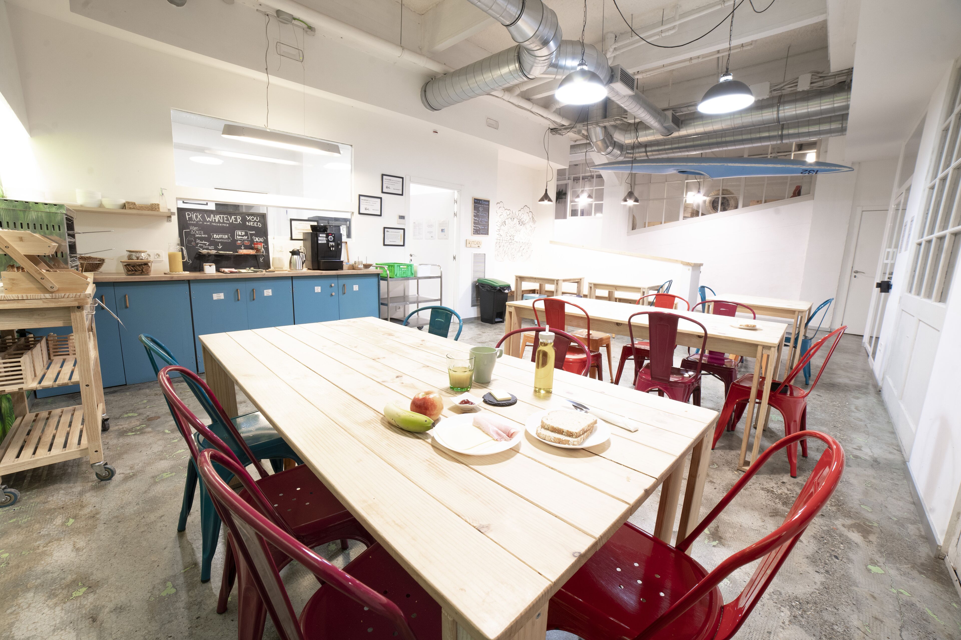 Una cocina amplia con una mesa de madera larga, sillas rojas y diversos electrodomésticos.