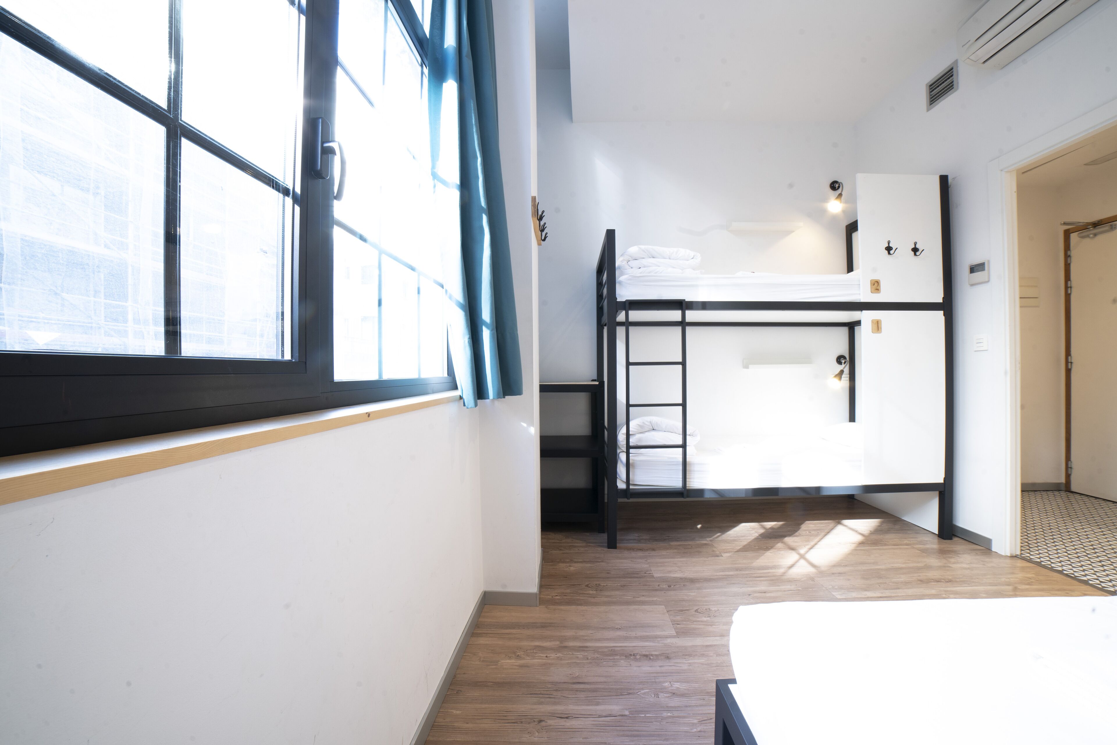 Een studentenkamer met een stapelbed, een raam met gordijnen en een deur.