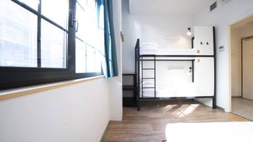 Een studentenkamer met een stapelbed, een raam met gordijnen en een deur.