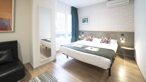 A modern bedroom with a large bed, a black leather chair, a mirror, and a view of the outdoors. - Koba Hostel (San Sebastián)